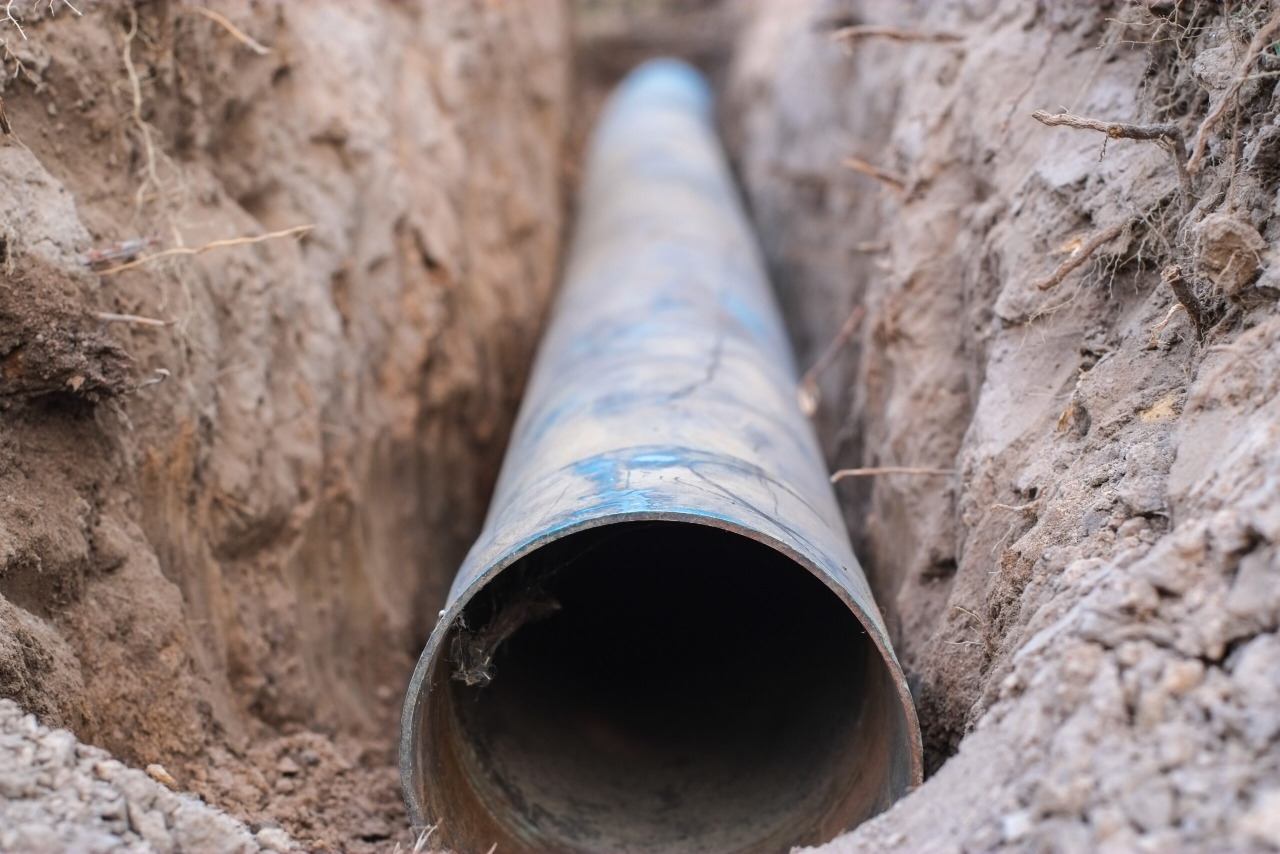 An underground sewer pipe rests in a freshly dug trench, ready for installation or inspection. The surrounding soil and visible pipe material highlight the scope of professional sewer line replacement or repair work typically performed by experienced plumbing contractors.