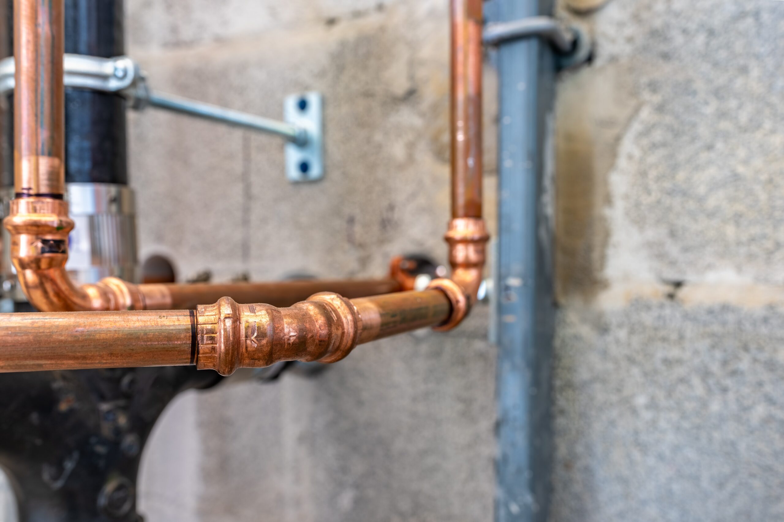 A close-up view of newly installed copper plumbing pipes against a concrete basement wall. The polished fittings and precise joints reflect professional craftsmanship and recent work. The image highlights quality materials and expert pipe installation, often associated with specialized plumbing services.