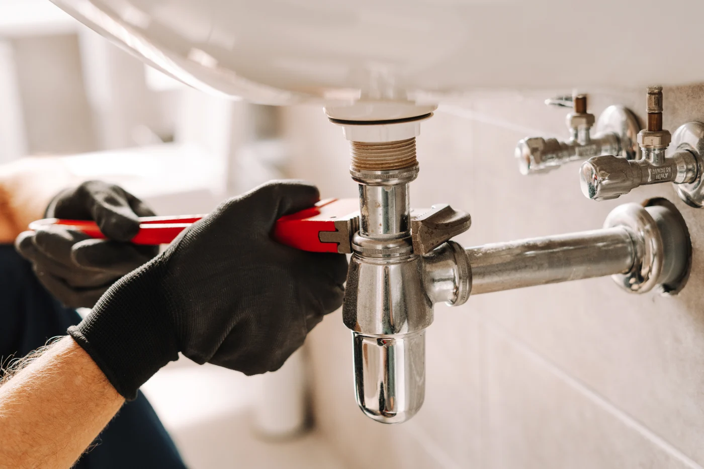 A gloved plumber tightening a