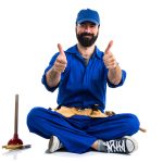 A happy plumber with a beard sitting cross-legged and holding two thumbs up against a white background.