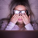 A woman rubbing her eyes as she researches plumbing companies on her laptop late at night.
