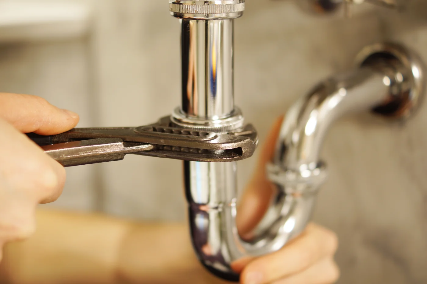 Close-up of a plumber tightening a bolt on a sink pipe.