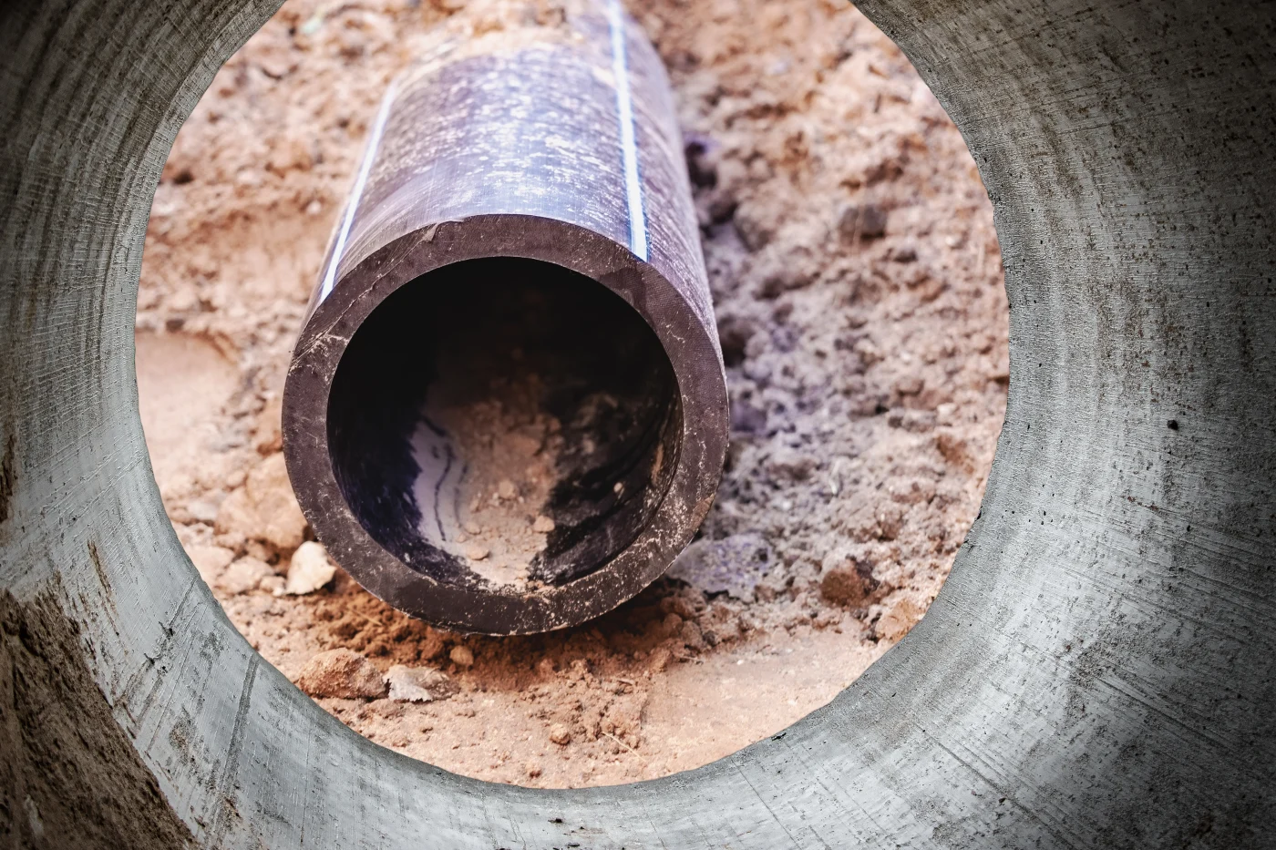 Outstanding Sewer Line Replacement in San Leandro, CA | Facilities Plumbing & Drain A view from a large pipe at a black sewer pipe in the dirt.