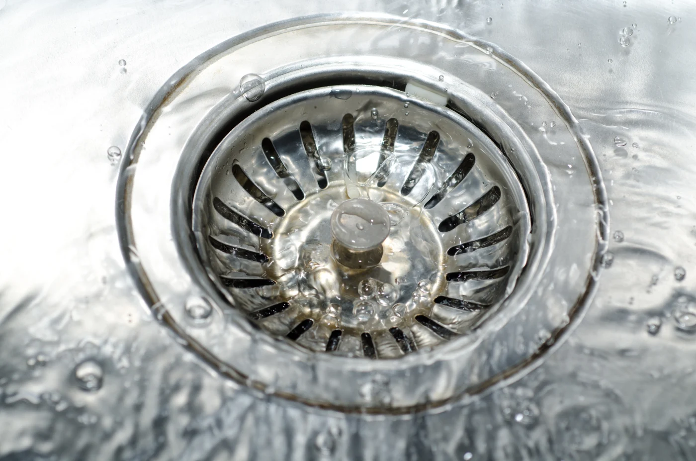 A clean drain in a stainless steel sink with running water.