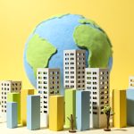 A paper-style earth with wood building models, building blocks, and paper trees against a yellow background.