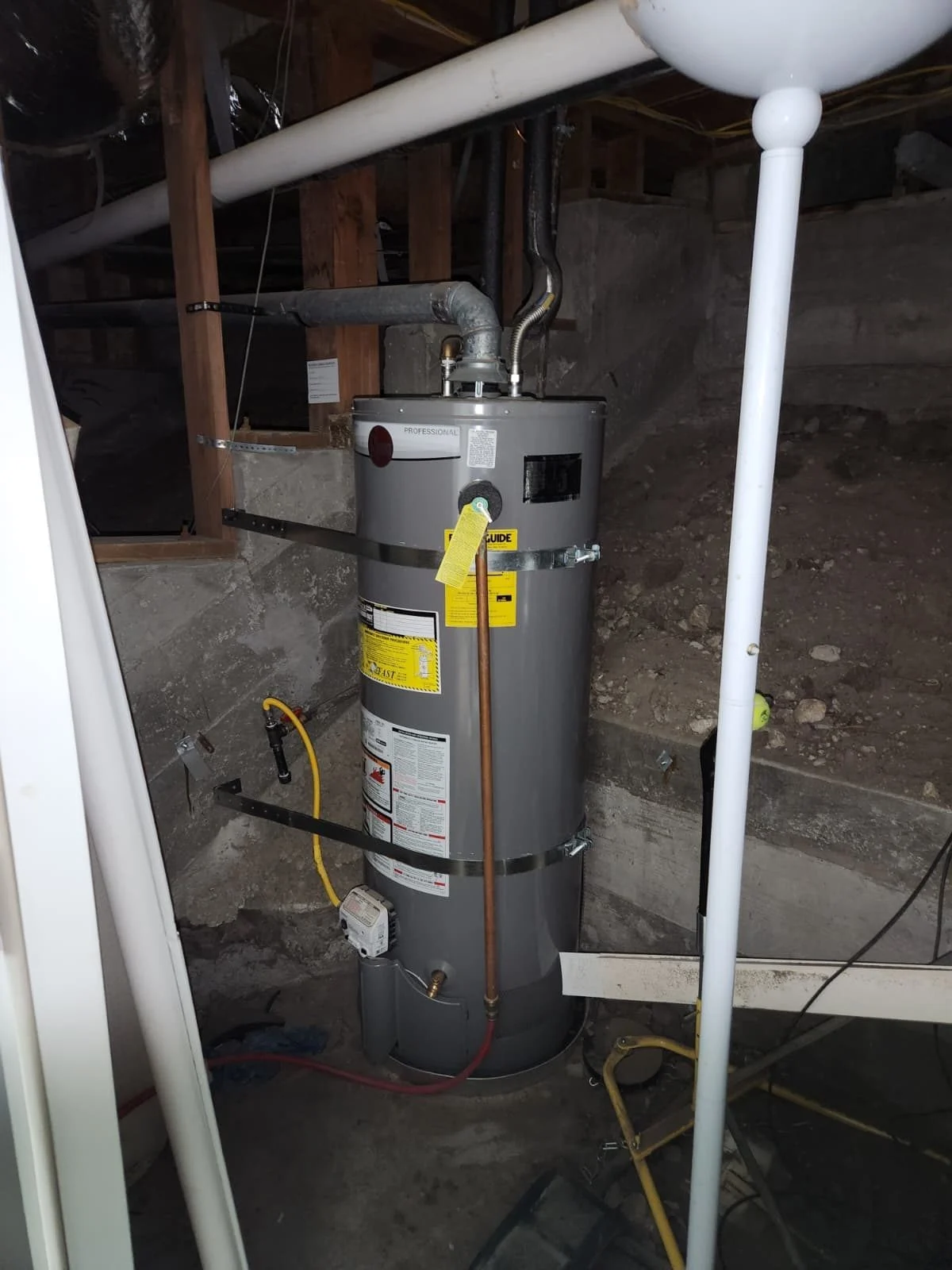 Water heater installed in a crawl space with copper piping, gas line, venting, and nearby plumbing lines visible.