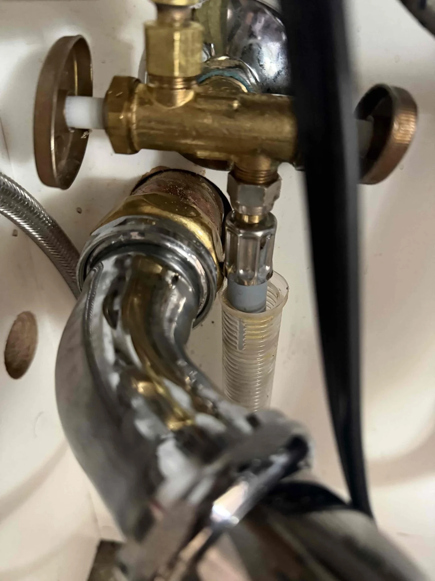 Close-up of under-sink drain piping, brass valve, and supply line connections during plumbing inspection or repair.