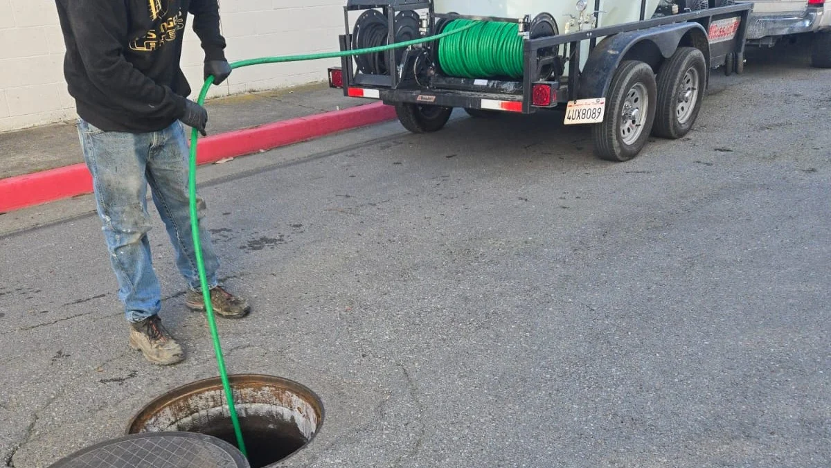 A worker feeds a hose into a manhole for sewer and drain-clog-clearing service.