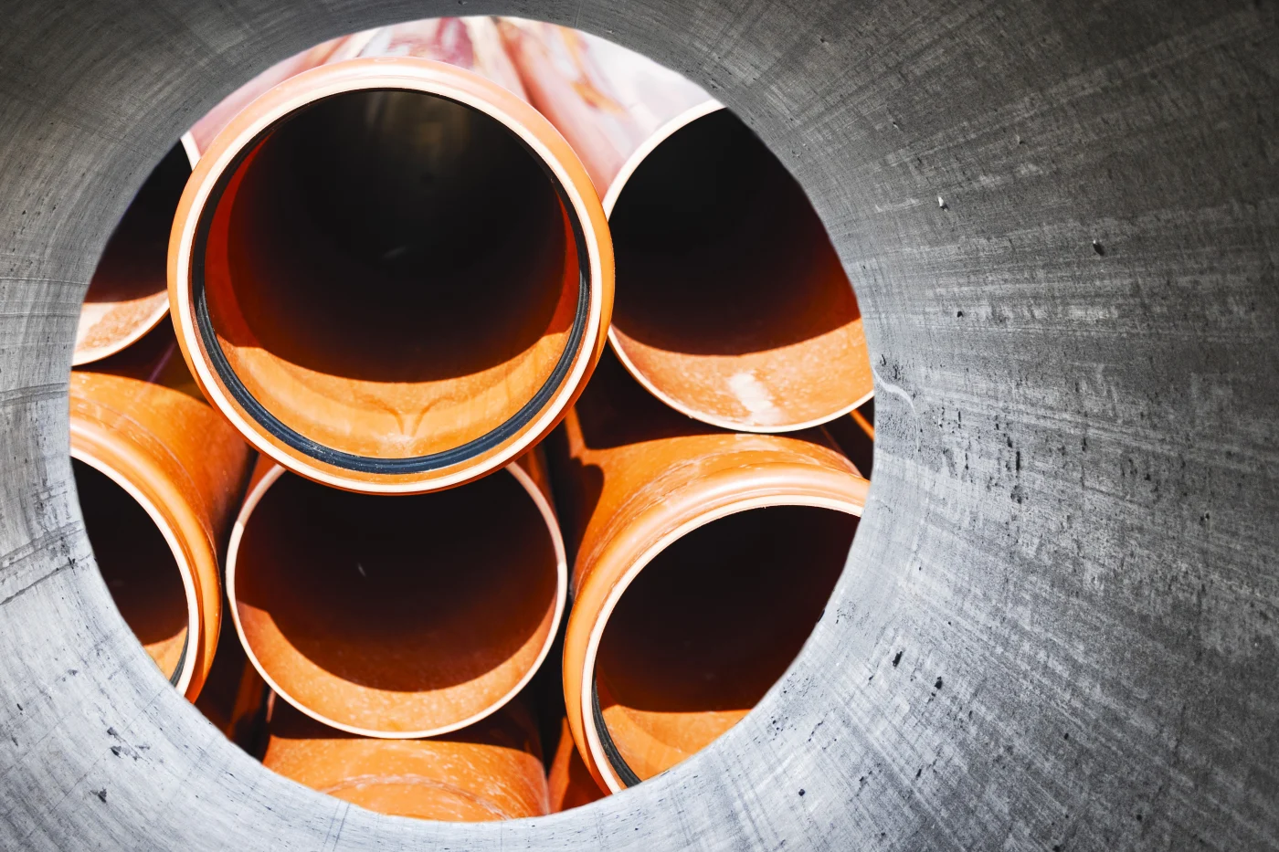 Orange commercial sewer replacement pipes stacked inside a gray pipe opening, showing black rubber gaskets, circular pipe ends, and rough plastic.